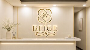A reception desk with a logo and the word 'BEIGE' on it, a vase with flowers, and a candle on the counter. - Beige Hotel (Ho Chi Minh City)
