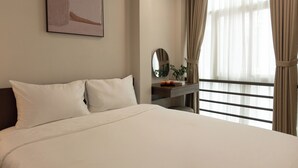 Une chambre d’hôtel avec un lit, une table de chevet dotée d’un miroir, une plante en pot et une fenêtre avec des rideaux.