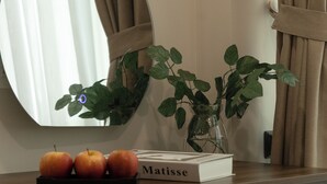 Un bureau en bois avec un miroir, un vase contenant des feuilles vertes et trois pommes.