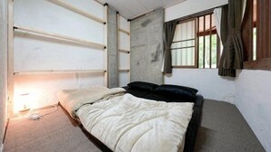 A single bed with a white comforter and black pillows in a room with a concrete wall and a window with curtains. - A private lodge where you can enjoy authentic BBQ surrounded by nature (Tsumagoi)