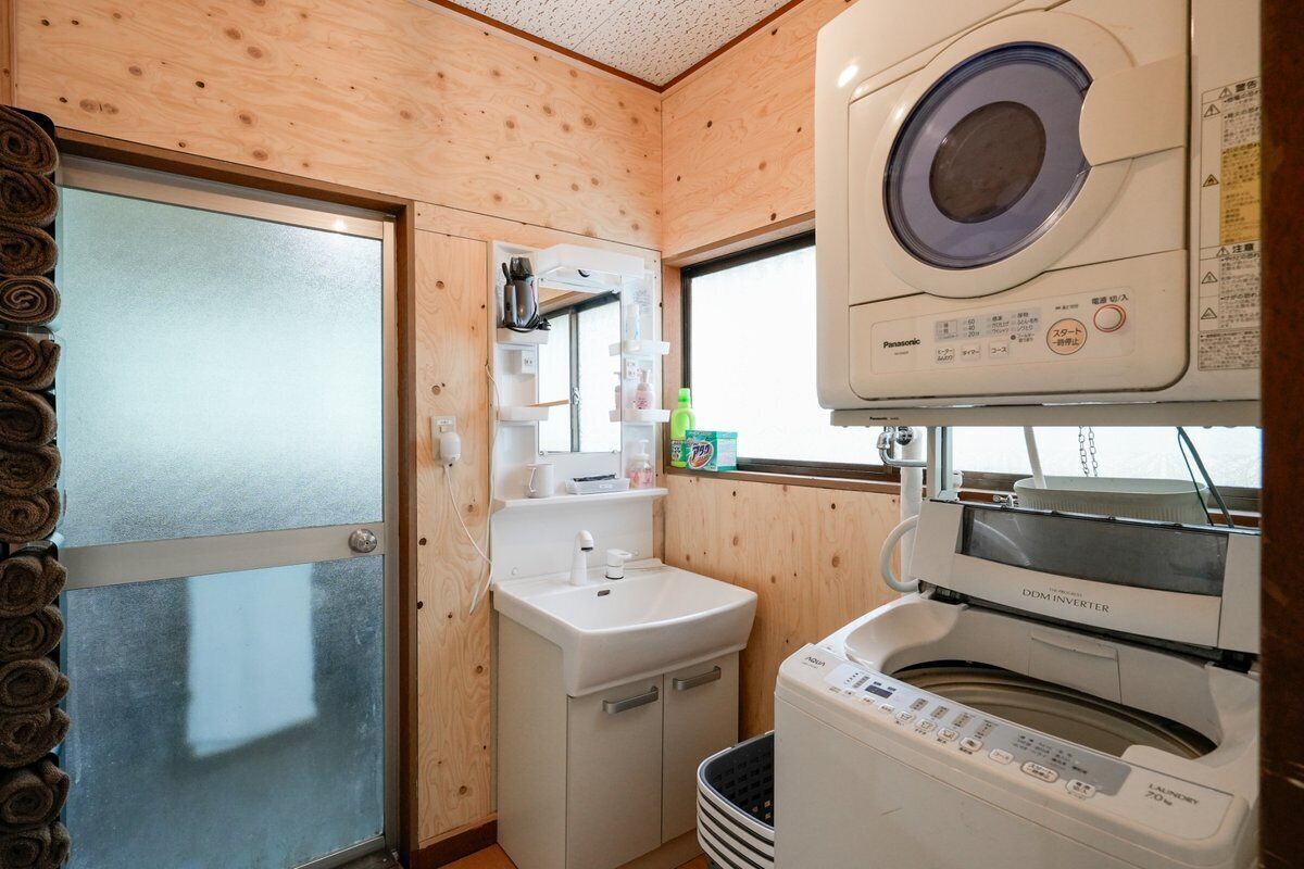 A compact room with a washing machine, a sink, and a door with a towel rack.