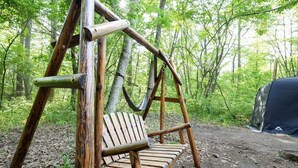 A wooden swing set in a forested area with a tent nearby.