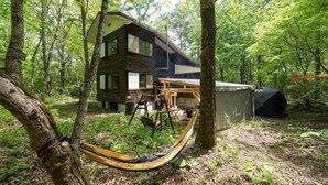 Une cabane dans une forêt, avec un hamac, une table et un barbecue.