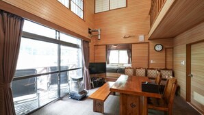 Une pièce spacieuse avec un décor intérieur en bois, une grande fenêtre, une table à manger avec des chaises, un canapé et un téléviseur.