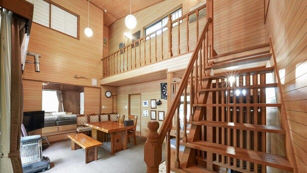 Une cabine spacieuse avec un plafond haut, des murs en bois, un coin repas, un salon avec un canapé et une télévision, et un escalier.
