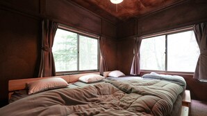 Une chambre confortable, aménagée dans le style d’un chalet, avec deux lits, des têtes de lit en bois et de grandes fenêtres dotées de rideaux.