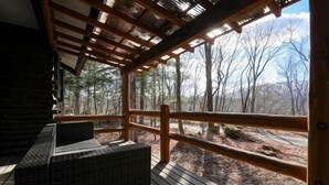 A covered outdoor deck with wooden railings and a bench, overlooking a forested area.
