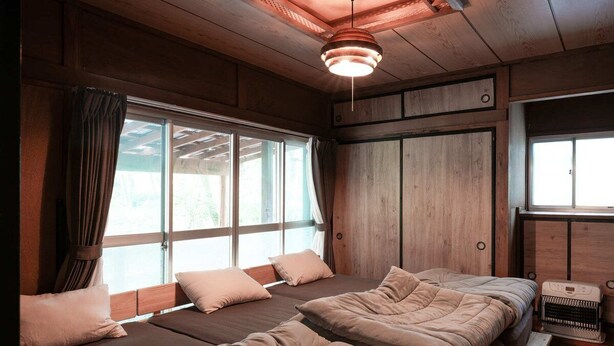 A room with a wooden ceiling, large windows, and a bed with multiple pillows.
