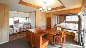 A compact RV kitchen with a wooden table and bench, a built-in stove, and a window with curtains.