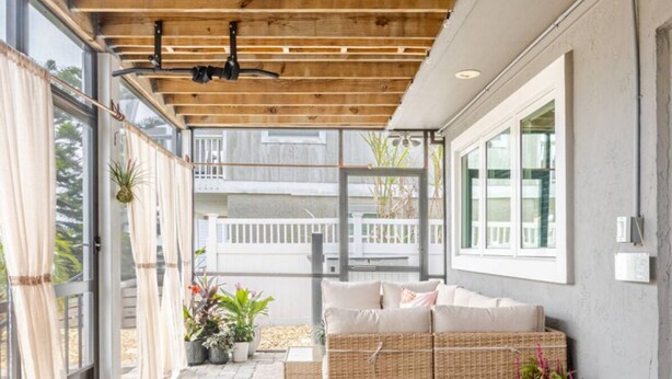 Ein überdachter Patio-Bereich mit Deckenventilator, Rattanmöbeln, Topfpflanzen und Steinplattenboden.