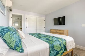 Une chambre à coucher comprenant un lit, une armoire, un téléviseur et une salle de bain visible à travers une porte ouverte.