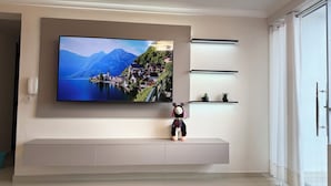 Ein modernes Wohnzimmer mit einem flachbildfernseher an der Wand, einem weißen Konsolentisch darunter und einem kleinen dekorativen Gegenstand auf dem Tisch.