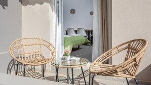 Een balkon met rieten stoelen, een glazen tafel en uitzicht op een kamer met een bed en een groene deken.