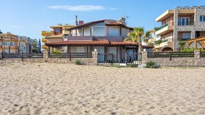 Een strandhuis met een tweelaags gebouw, een stenen muur en een zandstrand.