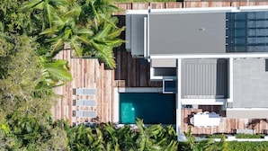 Ett modernt hus med en swimmingpool, ett trädäck och frodig grönska.
