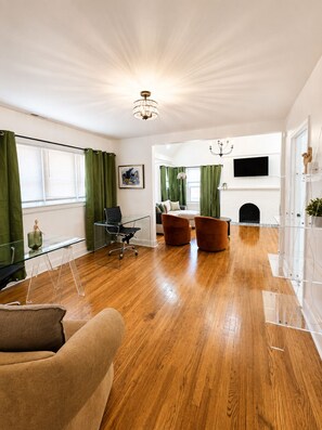 A spacious living room with a wooden floor, a dining area with two chairs, a sofa, and a fireplace. - Dogs Welcome!  Fun, Stylish Detroit Tudor w/ Fenced Yard! (Detroit)