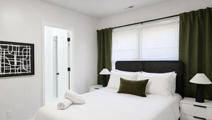 Un dormitorio moderno con una cama grande, mesitas de noche, una obra de arte en la pared y una ventana con cortinas.