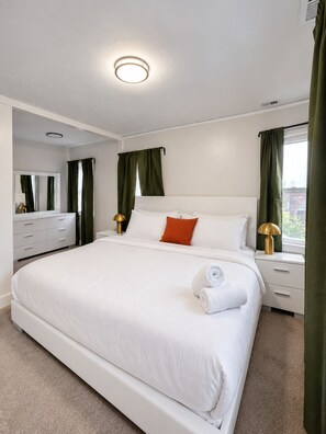 A hotel room with a large bed, a bedside table with a lamp, a dresser, and a window with curtains. - Dogs Welcome!  Fun, Stylish Detroit Tudor w/ Fenced Yard! (Detroit)