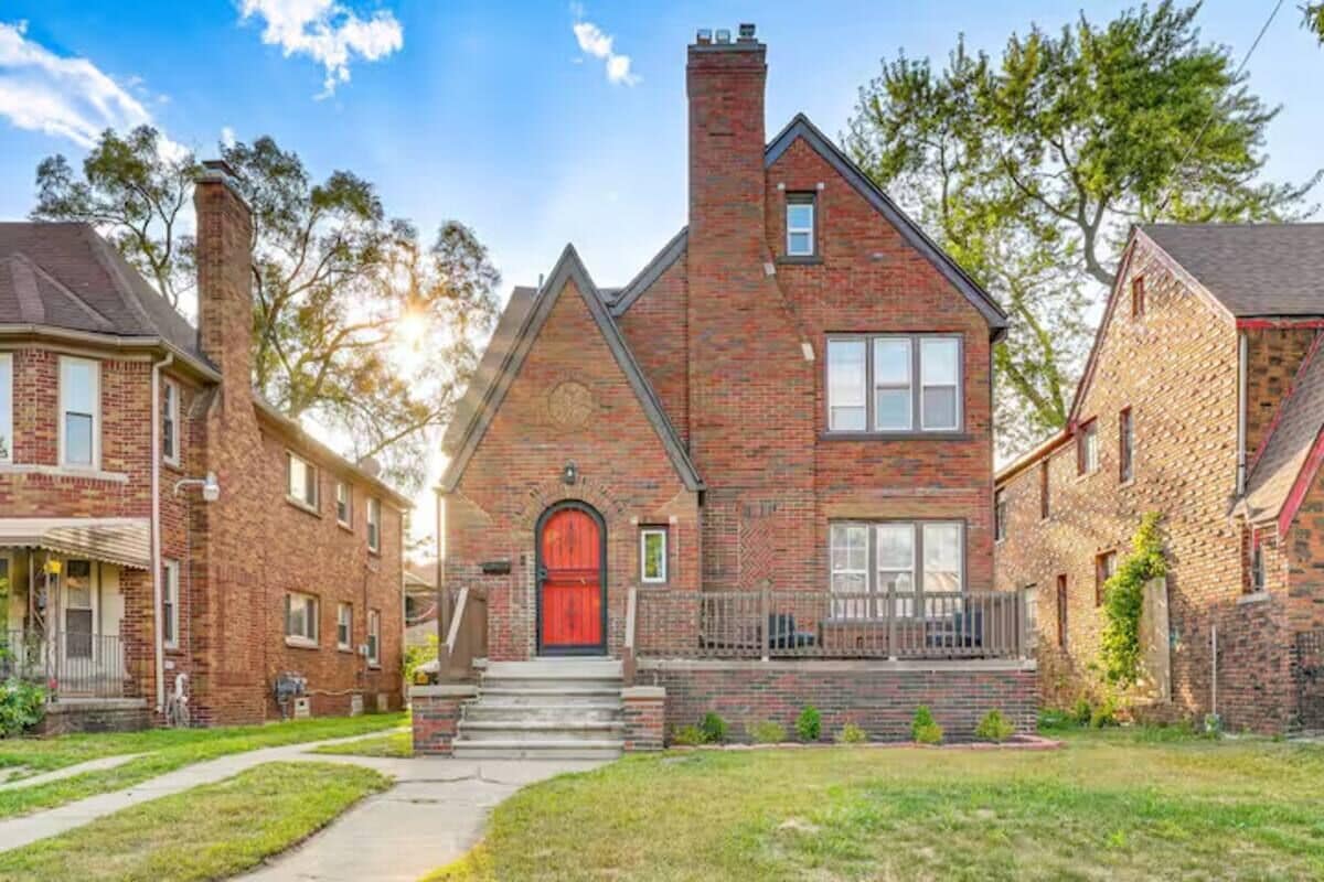A two-story brick house with a red front door, a chimney, and a small porch.