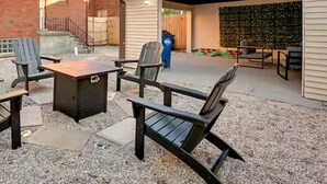 Un patio exterior con un pozo de fuego, sillas tipo Adirondack y una zona de estar cubierta.