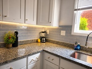A kitchen with white cabinets, a granite countertop, a blender, a potted plant, and a window with a view of a brick wall. - Dogs Welcome!  Fun, Stylish Detroit Tudor w/ Fenced Yard! (Detroit)