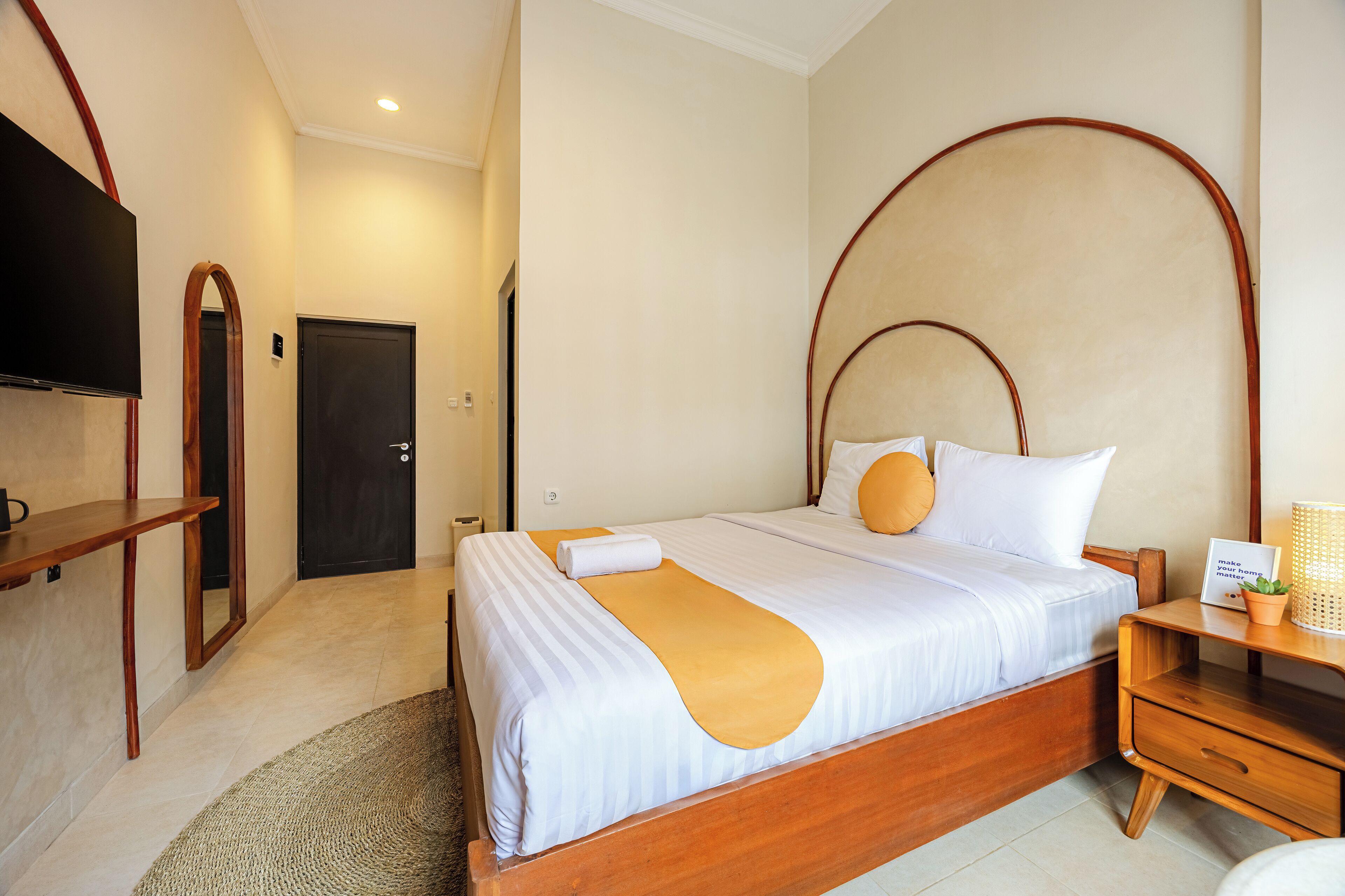 A hotel room with a large bed, wooden headboard, a bedside table with a lamp, and a TV mounted on the wall.