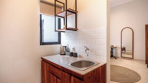 A modern kitchen with a wooden cabinet, a stainless steel sink, and a window above the counter. - Cove Chara (Jimbaran)