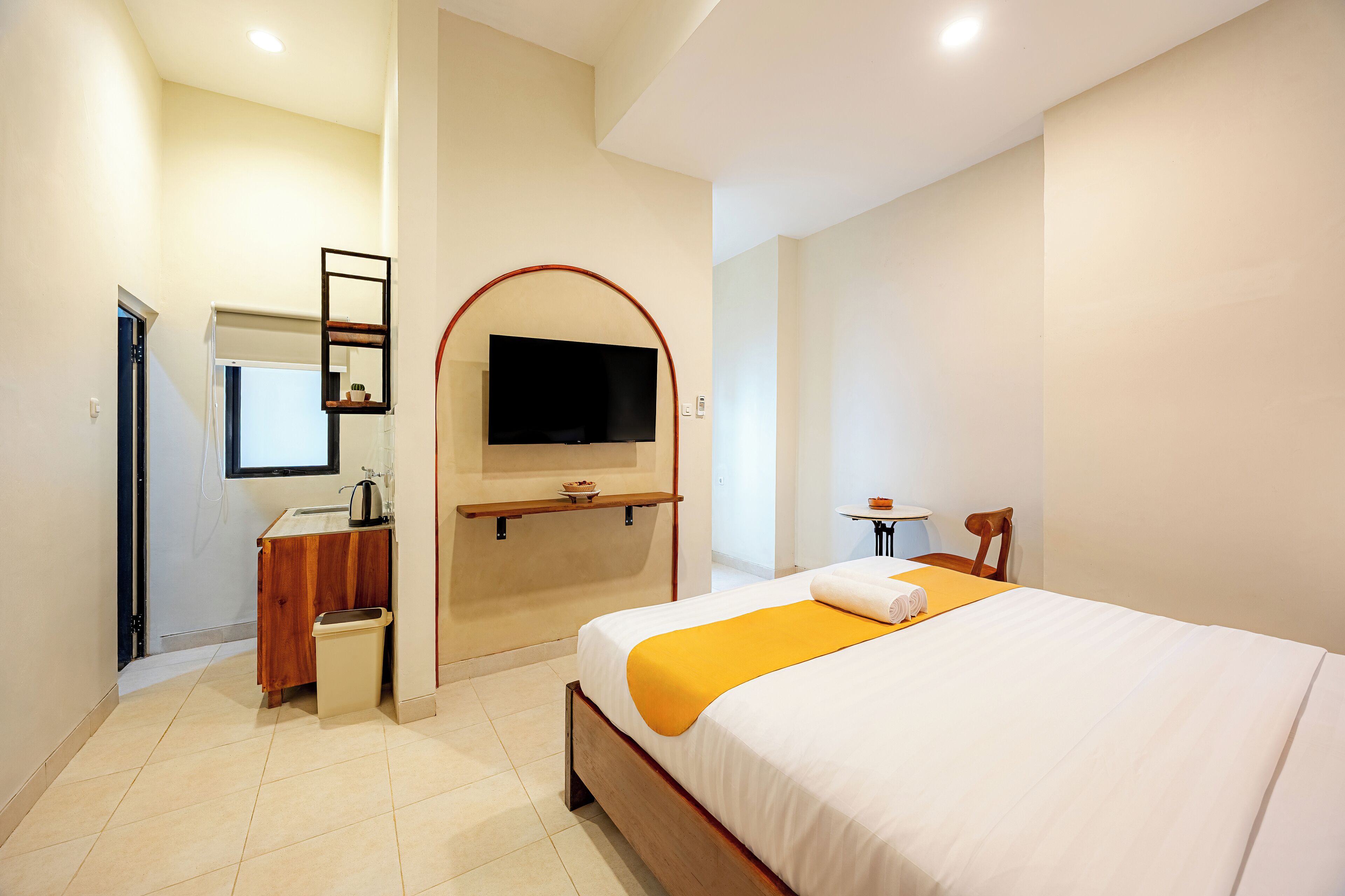 Una habitación de hotel con una cama, un televisor en la pared, una mesita pequeña y una silla.