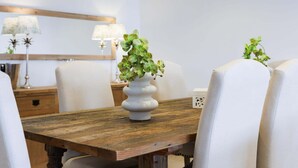 Uma mesa de jantar com um vaso branco de orquídeas verdes, cadeiras de madeira e um aparador de madeira com luminárias.