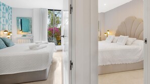 Quarto moderno com duas camas, banheiro e varanda florida.