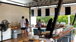 An outdoor dining area with a long table set for service, a fan, and a brick wall. - Lastsearesort (Koh Lan)