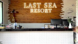 A reception desk with a wooden panel displaying 'LAST SEA RESORT' and a black counter with various items. - Lastsearesort (Koh Lan)