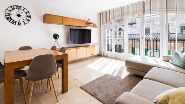 Een moderne woonkamer met een eethoek, een groot raam met uitzicht en een wandklok.