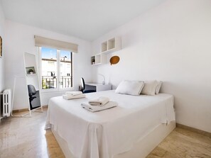 Quarto de hotel com uma cama grande, uma escrivaninha, uma cadeira e vista para a cidade pela janela.
