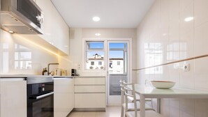 Een moderne keuken met witte kastjes, een ingebouwde oven en een eethoek met een glazen tafel en witte stoelen.