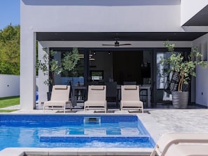 Ein moderner Poolbereich im Freien mit Liegestühlen und einem Esstisch.