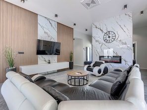Ein modernes Wohnzimmer mit einer Eckcouch, einem Flachbildfernseher, einem Kamin und einer Marmorwand.