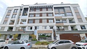 Un edificio residencial de varios pisos con balcones, una tienda y coches aparcados.