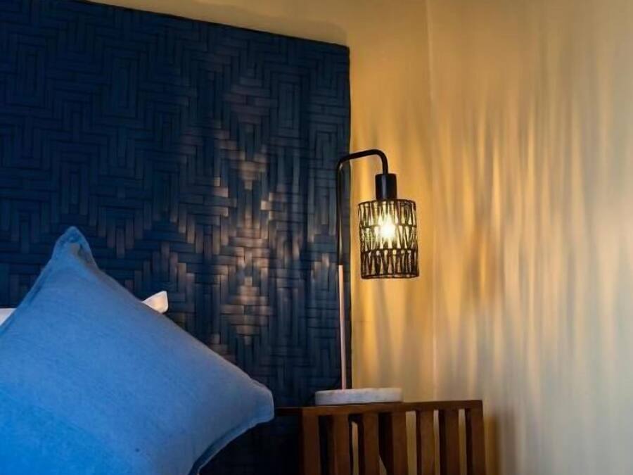 A neatly made bed with a blue pillow, a wooden nightstand, and a wall-mounted lamp.