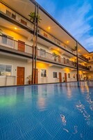 Un hotel de varios pisos con una amplia piscina cubierta, balcones con barandillas y plantas en macetas.