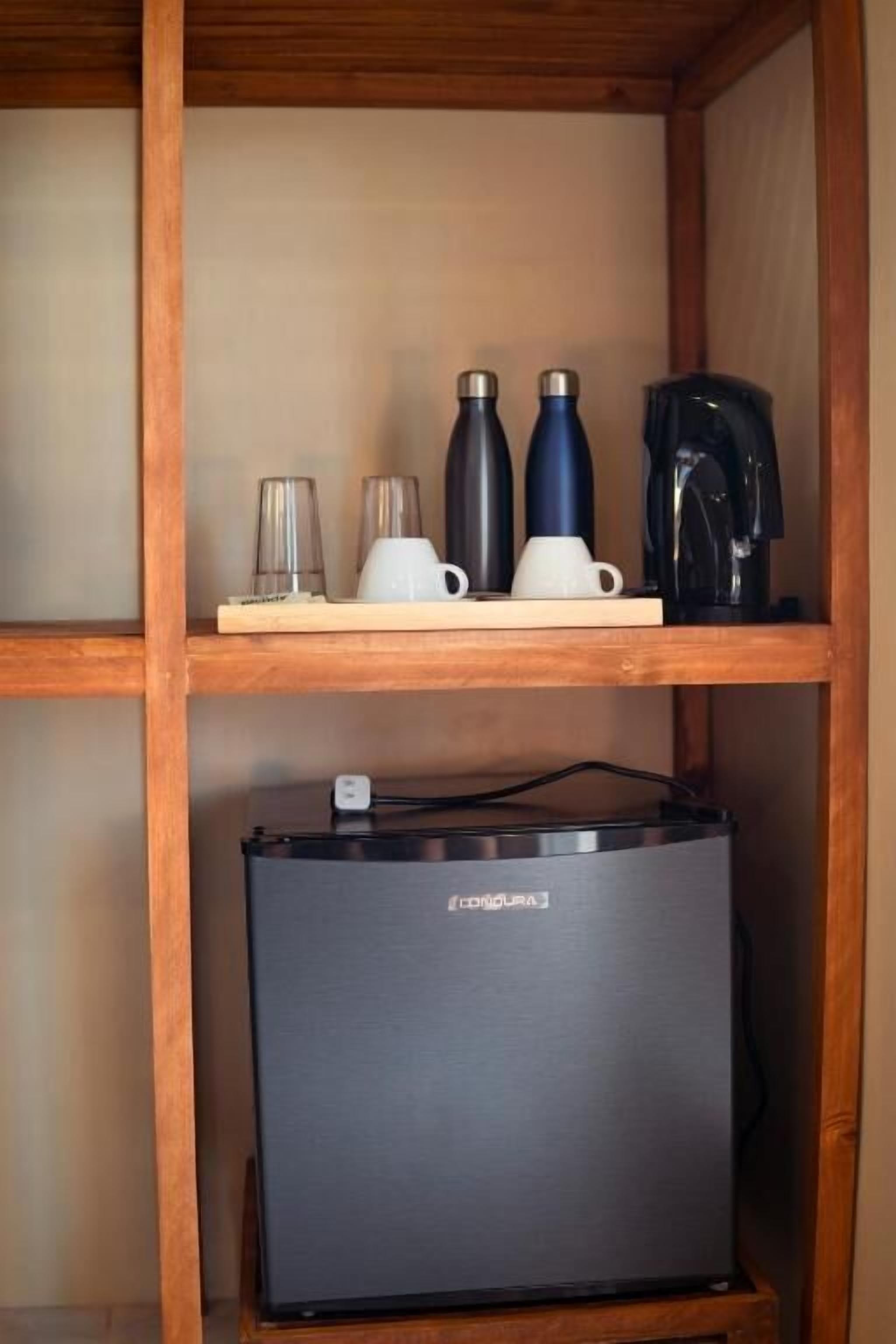 Uno scaffale di legno con una macchina da caffè, due thermos e due tazze. In basso, si vede una valigia nera.
