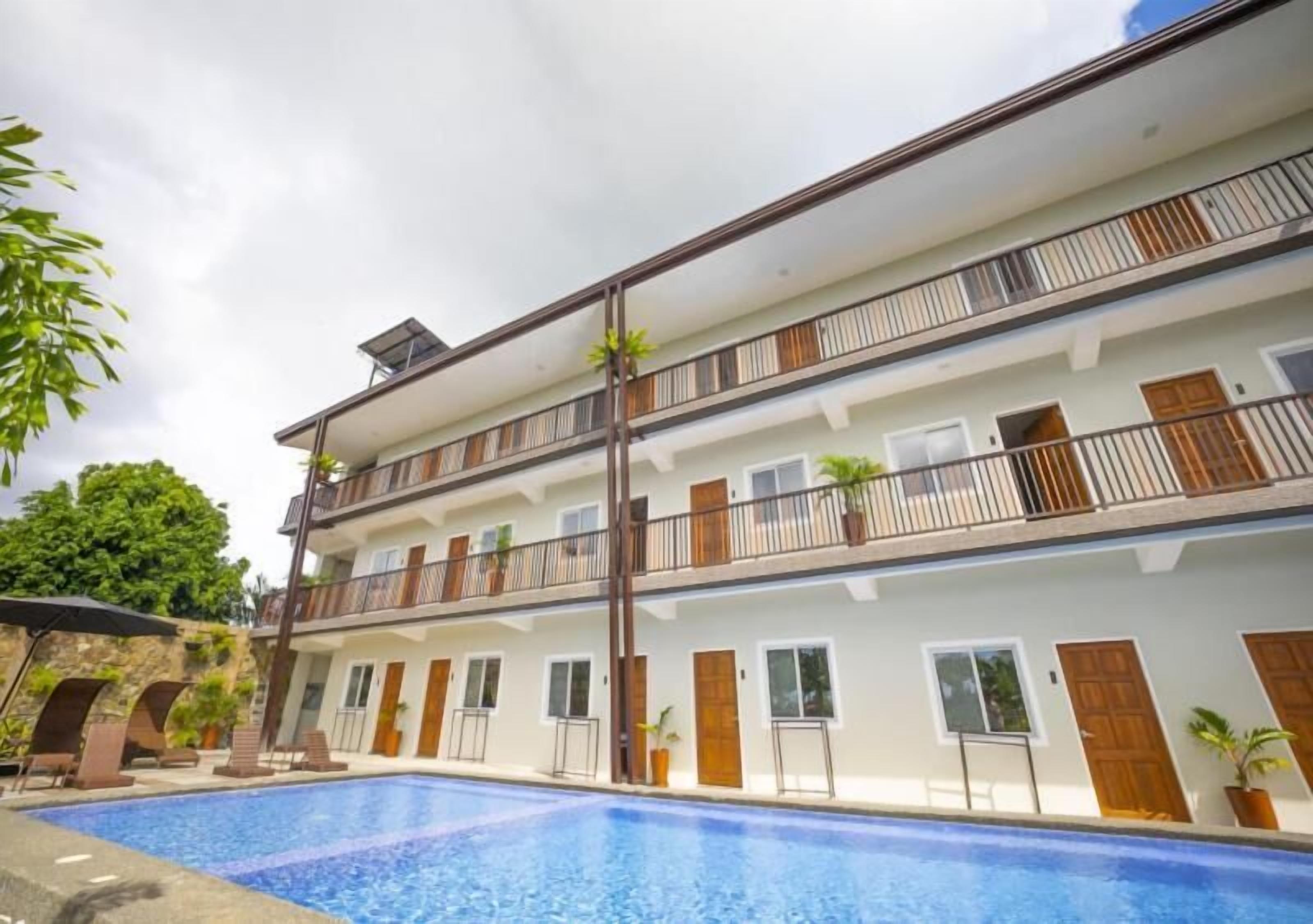 A multi-story hotel with a swimming pool, balconies, and potted plants.