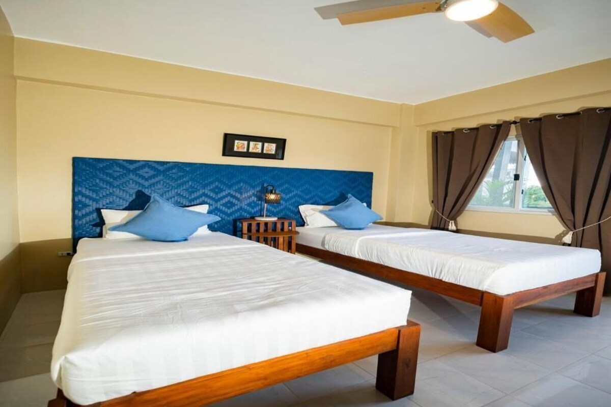 A hotel room with two beds, a ceiling fan, and a window with curtains.