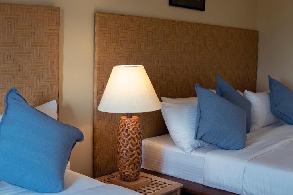 Ett hotellrum med två sängar, en sänggavel med mönster och en bordslampa.