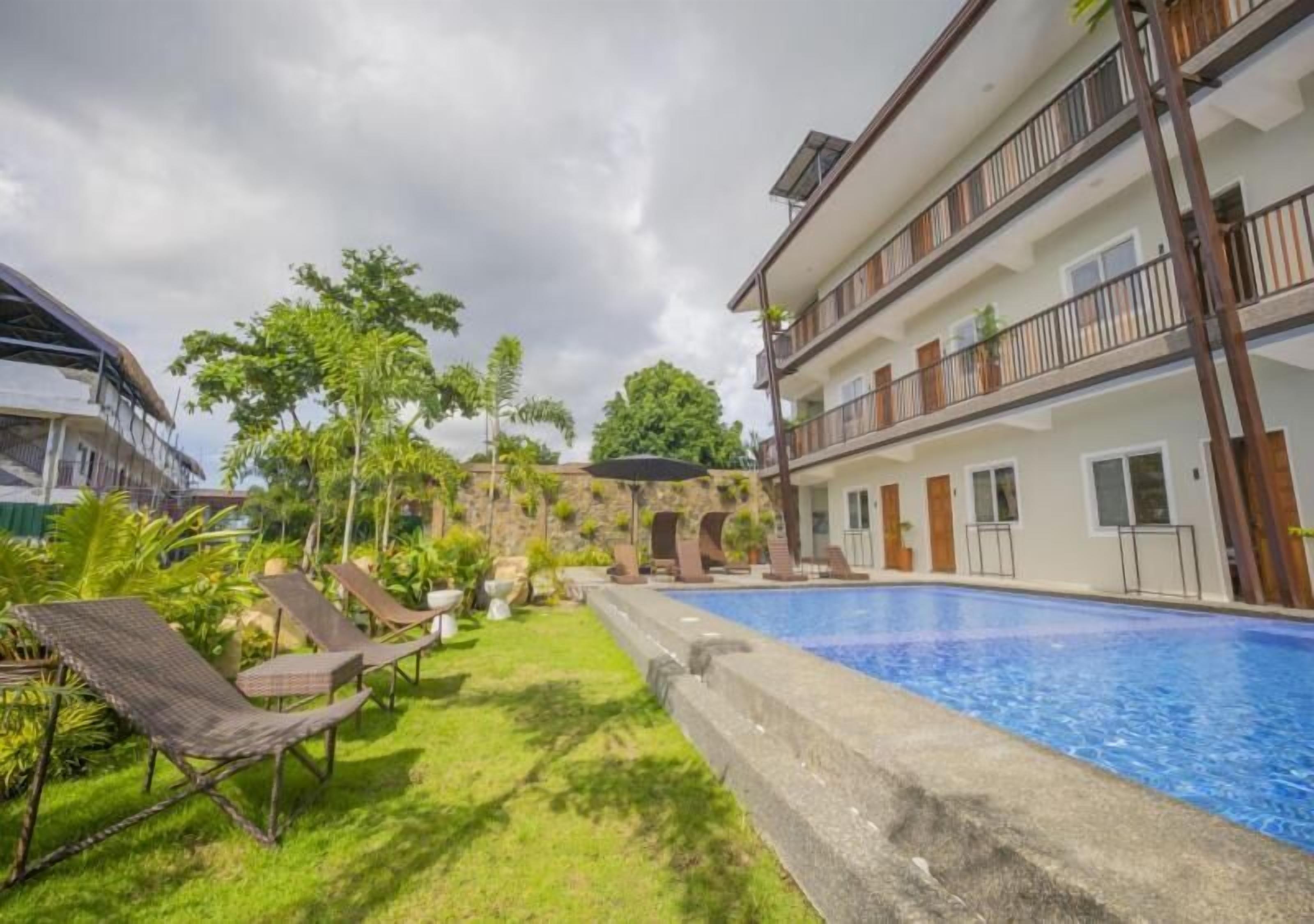 A hotel with a swimming pool, lounge chairs, and a garden area.