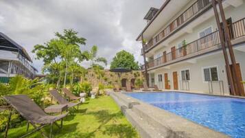 A hotel with a swimming pool, lounge chairs, and a garden area.