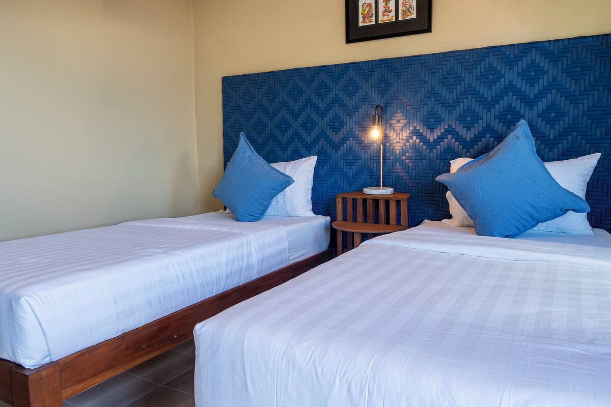 A hotel room with two single beds, a nightstand with a lamp, and a patterned headboard.