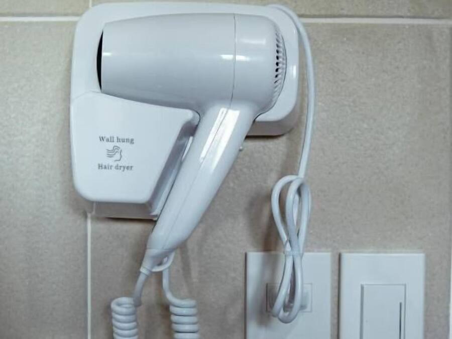 A wall-mounted hair dryer with a cord, connected to a power outlet.