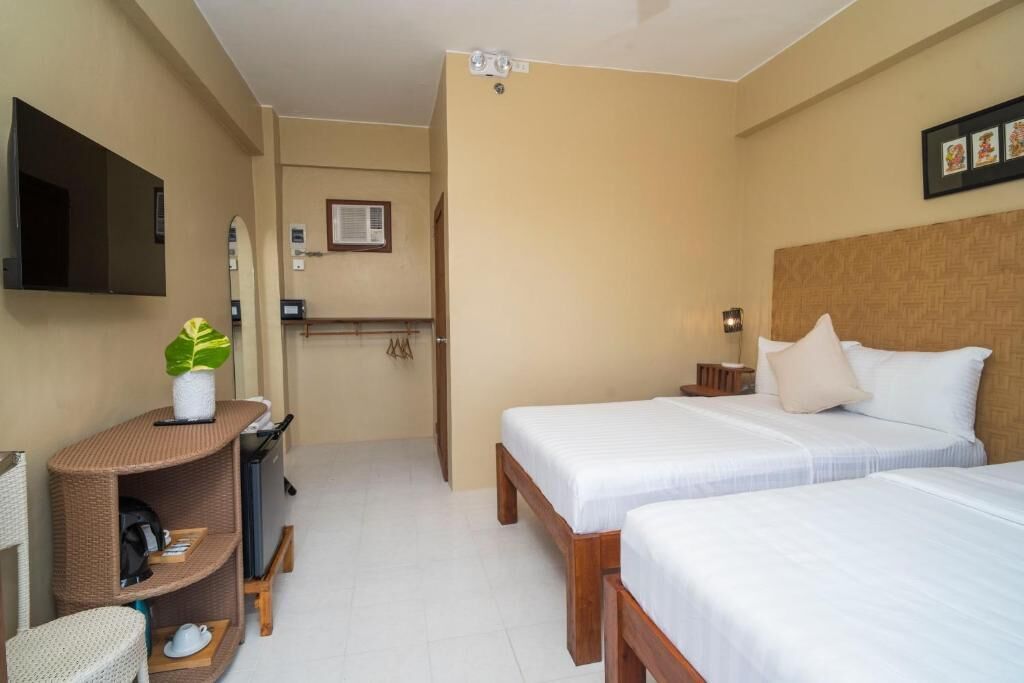A hotel room with two beds, a TV, a small desk with a plant, and a mirror.