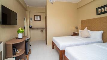 A hotel room with two beds, a TV, a small desk with a plant, and a mirror.